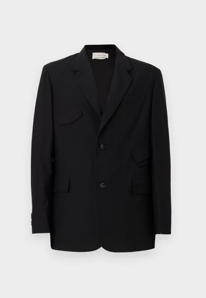 Blazer noir avec un design structuré, deux poches avant, deux boutons et une texture de tissu distincte avec des détails superposés.