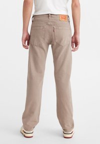 Pantalons en denim beige avec une coupe décontractée, dotés de poches arrière, d'une étiquette de marque rouge sur la ceinture et de détails matériels minimaux.