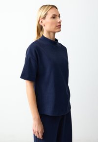 Marineblaues Kurzarmoberteil mit hohem Kragen, aus strukturiertem Stoff gefertigt. Verfügt über ein schlichtes Design und eine lockere Passform, die sich gut für die Freizeit eignet.