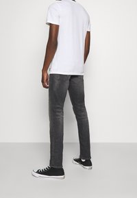 Jeans gris de corte slim, mezcla de algodón, con un acabado ligeramente desgastado. Combinados con una camiseta blanca de cuello redondo y zapatillas negras de caña baja.