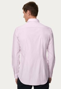 Lichtroze langemouwen shirt met een klassieke kraag, rugdetail en afgeronde zoom; de gladde textuur en knoopmanchetten zijn zichtbaar.