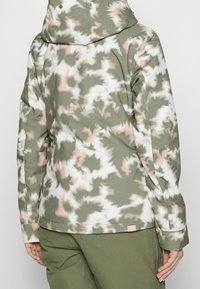 Blumenmusterjacke in gedämpftem Grün, Weiß und hellrosa. Sie hat eine Kapuze, lange Ärmel und ein kleines Markenetikett am Saum.