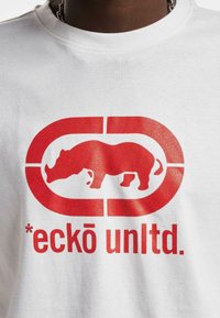 Balta medvilninė marškinėlių su dideliu raudonu rhinocero grafiku ir tekstu "*eckō unltd." po dizainu. Paprasta apvalia iškirpte.