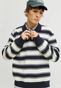 Proužkovaný pulovr s námořnickými, krémovými a šedými pruhy. Má límec typu polo a žebrované manžety. Vyrobeno z měkké látky, volný střih.