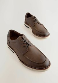 Zapatos de cuero marrón con un acabado suave, diseño con cordones, suela blanca contrastante y costura elevada a lo largo del borde.