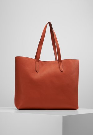 Braune Leder-Shopper-Tasche mit zwei langen Henkeln, präsentiert auf einem weißen Podest vor einem schlichten grauen Hintergrund.