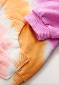 Primer plano de puños acanalados y aperturas de bolsillos en tejido tie-dye suave en colores naranja, rosa, blanco y púrpura.