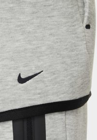 Shorts atletici grigi realizzati in tessuto misto cotone. Presentano un logo Nike nero e una vita nera con righe verticali. Superficie strutturata.