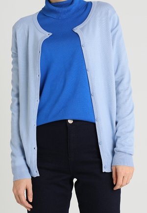 Lichtblauw vest met een ronde hals, knopen aan de voorkant, geribbelde manchetten, gedragen over een blauwe coltrui, gecombineerd met donkere broek.