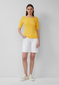 Haut à manches courtes côtelé jaune associé à un short blanc à ourlet roulé et des baskets légères. Design simple, texture douce et contraste de couleurs vives.