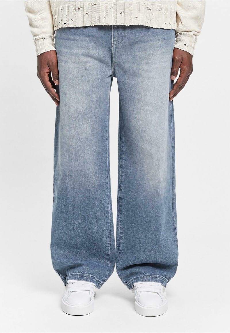 Lyseblå vide jeans med en falmet finish, der har høj talje, rå kant og subtil tekstur. Sammen med hvide sneakers.