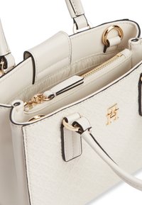 Κρεμ τσάντα χειρός με υφασμένο μοτίβο, χρυστό φερμουάρ, χρυσό έμβλημα λογότυπου και διπλές λαβές με χρυσά μέρη.