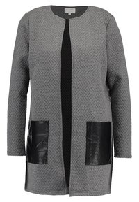 Pitkä harmaa teksturoitu neuletakki, jossa on musta keskipaneeli ja kaksi suurta mustaa nahkasta etutaskua, jossa on pyöreä pääntie ja pitkät hihat.