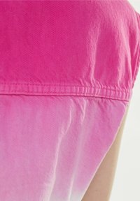 Tessuto di denim rosa con un design ombre che sfuma dal rosa brillante a tonalità più chiare. Presenta una cucitura visibile e una consistenza morbida.