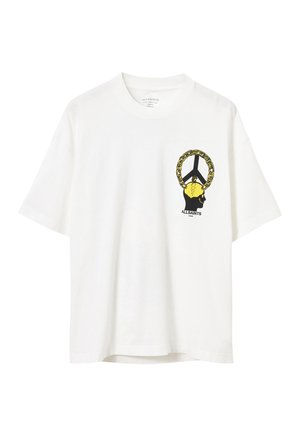 Vit bomulls t-shirt med en svart och gul grafik av ett ansikte med en kedja, placerad på den vänstra bröstområdet. Korta ärmar.