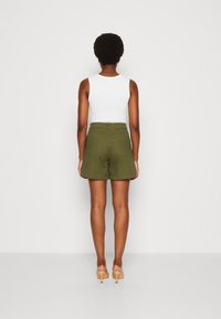 Shorts vert olive à coupe ample, dotés de deux poches arrière et d'un ourlet cousu, associés à un débardeur blanc uni.