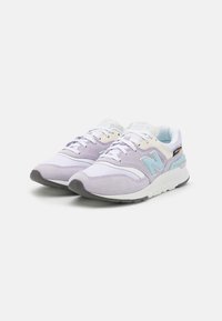 Un paio di sneaker New Balance di colore viola chiaro e bianco con logo "N" blu, lacci bianchi e suole grigie su uno sfondo bianco.