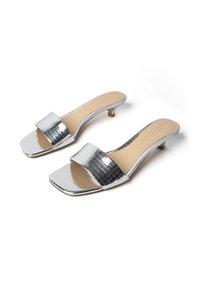 Sandales argentées à talons bas avec larges brides texturées et bouts carrés ouverts sur fond blanc.