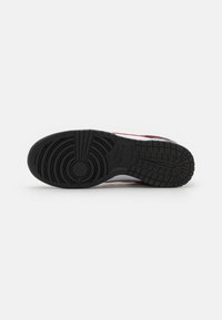 Semelle en caoutchouc noir d'une sneaker rouge et blanche avec des motifs de bande de roulement circulaires et en grille, avec un logo Nike près de la voûte plantaire.