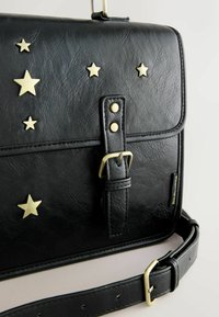 Czarna torba z syntetycznej skóry z klapką, złotymi gwiazdkowymi ćwiekami, odpinanym paskiem oraz fakturowaną powierzchnią z akcentem w postaci klamry.