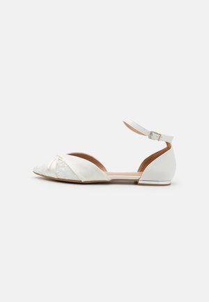 White flat shoes with an ankle strap, featuring a silky fabric and lace detail at the toe, complemented by a small bow and a solid sole.