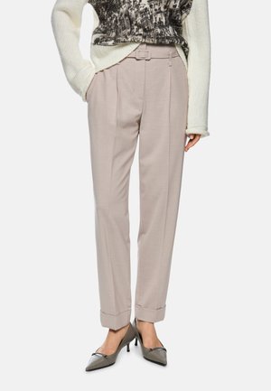 Beige Hosen mit Falten, Gürtelschlaufen und Umschlägen, kombiniert mit einem strukturierten cremefarbenen Pullover und grauen spitz zulaufenden Absätzen.
