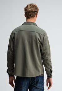 Olivengroene shirt met lange mouwen, een puntige kraag en knoopmanchetten. Heeft zichtbare stiksels en een losse pasvorm, gemaakt van zachte stof.