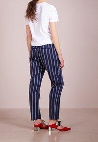 Bílé tričko s krátkým rukávem, modré pruhované kalhoty a červené boty na špičce se stříbrnými blokovými podpatky. Důraz na čisté linie a moderní střih.