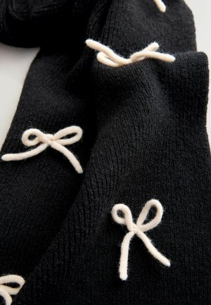 Black knit scarf featuring white yarn bow accents. The textured fabric displays a soft, woven pattern, highlighting the contrasting details.