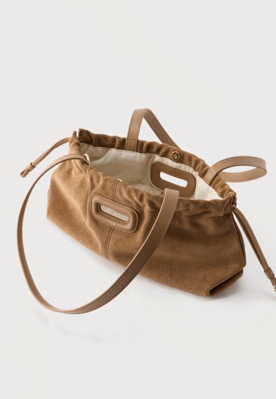 Καφέ τσάντα σουέτ με δερμάτινες λαβές και κλείσιμο με κορδόνι, εσωτερικό από μπεζ ύφασμα και ορθογώνια λεπτομέρεια κοπής στα πλάγια.