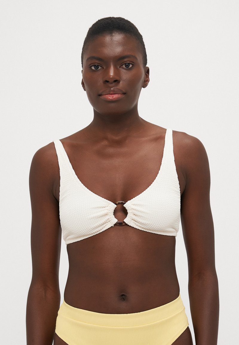 Haut de bikini texturé blanc avec un accent circulaire central, présentant de larges bretelles et un décolleté en V flatteur.