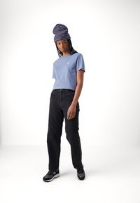 Lichtblauwe katoenen t-shirt, zwarte losse jeans en een multicolored gestreepte gebreide beanie. Zwarte hardloopschoenen met grijze en rode accenten.