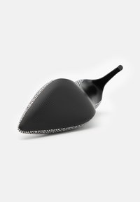 Høyhælte sko med spiss tå, svart teksturert materiale, og sølvdetaljer langs kanten. Skinnende svart hæl og intrikat design.