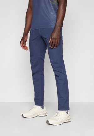 Navy blue fitted pants made of lightweight fabric with a smooth texture and subtle stitching details, paired with light athletic shoes.