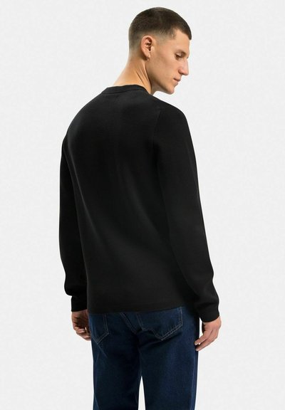 Sort sweater med lange ærmer, ribbet brystkant og en glat overflade. Båret med blå denim jeans. Set fra ryggen.