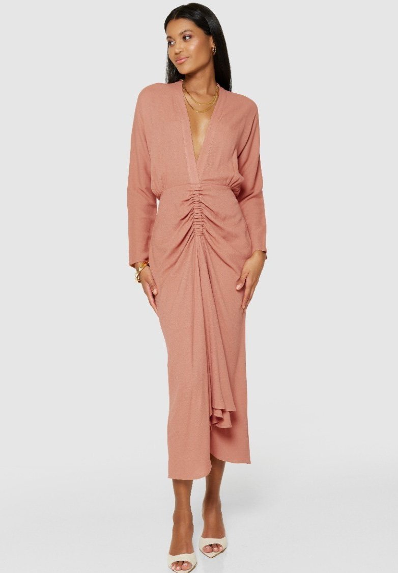 Roze jurk met een diepe V-hals, lange mouwen en geraffineerde details bij de taille, die halverwege de kuit reikt, met een vloeiende silhouet.
