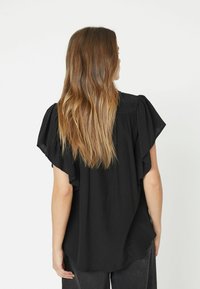 Blusa nera con maniche corte a volant, tessuto leggero, vestibilità rilassata e orlo curvo. Nessun motivo o dettaglio visibile.