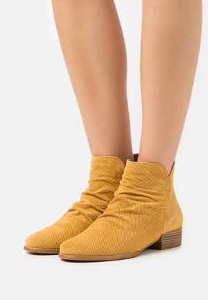 Botas de tobillo amarillas perforadas con un diseño holgado, tacón bajo apilado y tela texturizada. Presentan punta redondeada y acentos minimalistas.