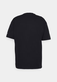 Svart t-shirt med kort ärm, rund hals, tillverkad av mjukt tyg, har platta sömmar och en liten vit logotyp på vänster ärm.