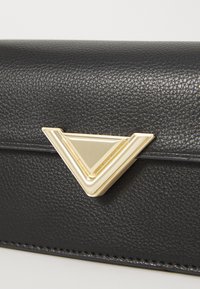 Black textured leather clutch with a gold triangular hardware accent. Compact shape, subtle stitching detail along the edges.