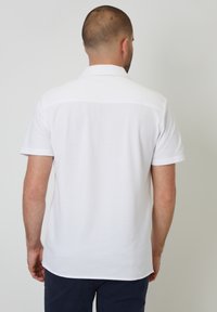 Polo shirt blanca de manga corta hecha de una mezcla de algodón, con una textura suave y un cuello clásico. La vista trasera muestra un diseño liso y un dobladillo recto.