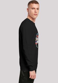 Sort sweatshirt med lange ærmer, der har et farverigt tegneserie-tema grafik foran. Glat tekstur, rund halsudskæring og tætsiddende manchetter.