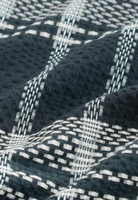 Tissu foncé avec un tissage gaufré texturé présentant un motif à carreaux blancs formant des lignes et des carrés entrecroisés.
