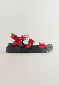 Red patent leather sandals with an adjustable double strap design, silver buckles, and a black rubber sole, featuring a chunky profile.