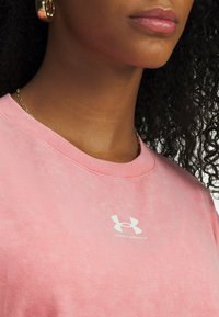 Camiseta de algodón rosa con cuello redondo y mangas cortas. Presenta un logo blanco en el pecho y una textura sutil en la tela.