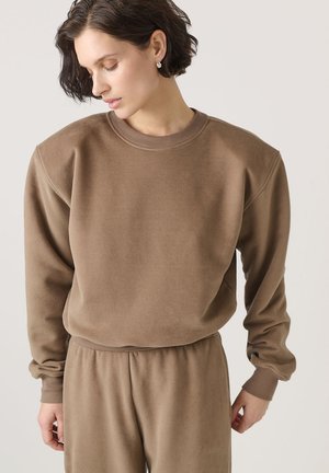 Hnedý sweatshirt s okrúhlym výstrihom a rebrovanými manžetami. Vyrobený z mäkkého materiálu, má voľný strih a je spárovaný s rovnakými nohavicami.