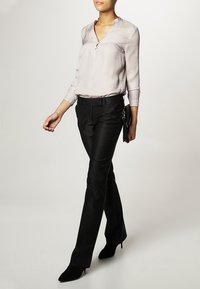 Ljusbeige silkblus med v-ringning, långa ärmar och en subtil lyster, kombinerad med skräddarsydda svarta byxor och spetsiga svarta klackar.