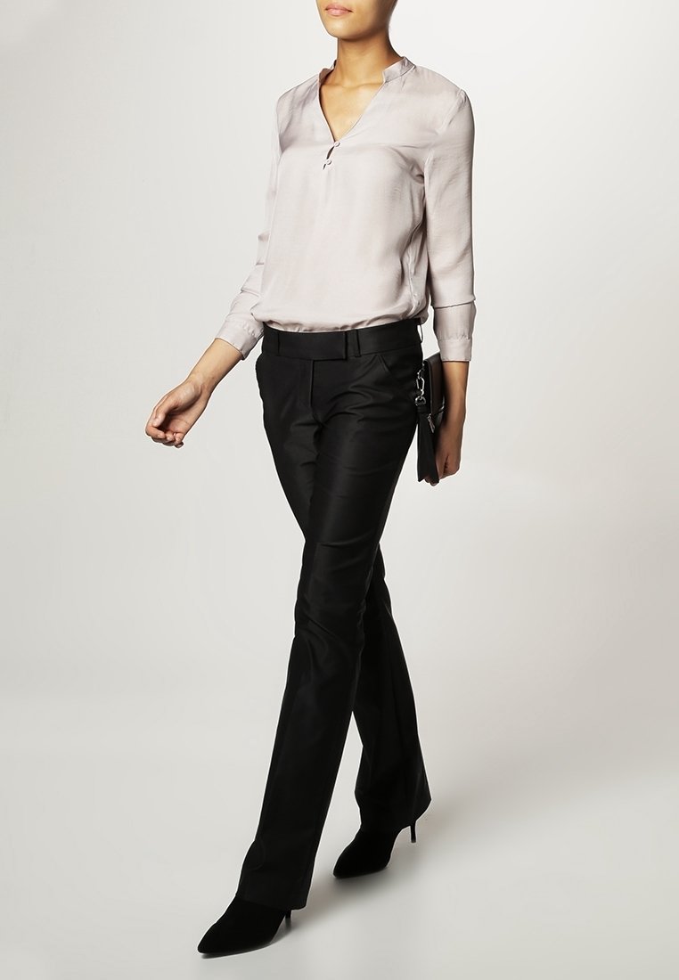 Ljusbeige silkblus med v-ringning, långa ärmar och en subtil lyster, kombinerad med skräddarsydda svarta byxor och spetsiga svarta klackar.