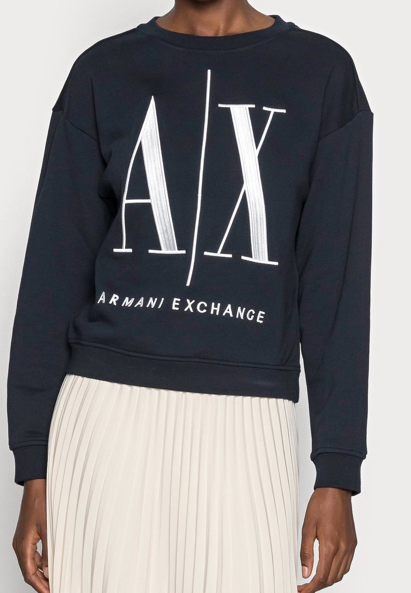 Tmavě modrá mikina s kulatým výstřihem, volným oversize střihem a bílým grafickým nápisem "A/X" a "ARMANI EXCHANGE" na přední straně.