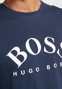 Laivastonsininen puuvillapaita, jossa on suuri valkoinen "BOSS" -teksti ja pienempi "HUGO BOSS" -teksti alla, klassisella pyöreällä kaula-aukolla.